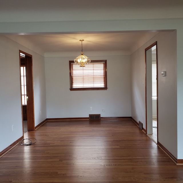 unfurnished room featuring dark wood-type flooring and an inviting chandelier