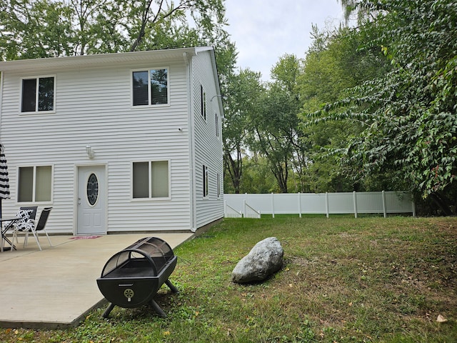 rear view of property featuring a yard, a patio, and an outdoor fire pit