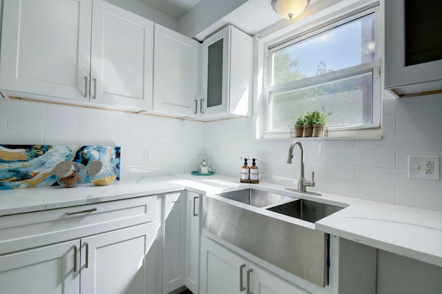 kitchen with light stone counters, backsplash, sink, and white cabinets