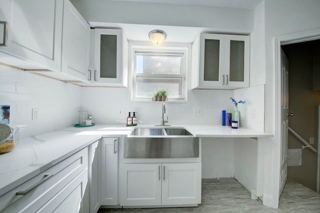 kitchen with white cabinetry, backsplash, light stone countertops, and sink