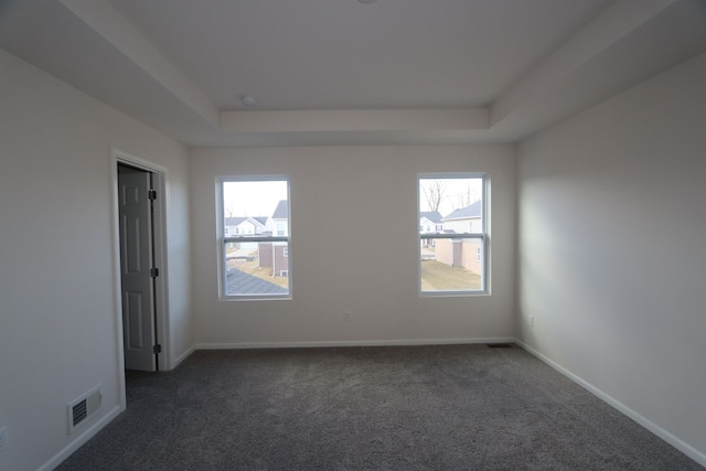 empty room featuring dark colored carpet, visible vents, a raised ceiling, and baseboards