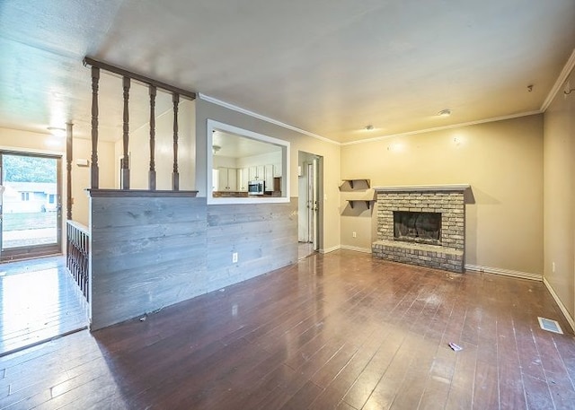 unfurnished living room featuring wood-type flooring, ornamental molding, and a brick fireplace