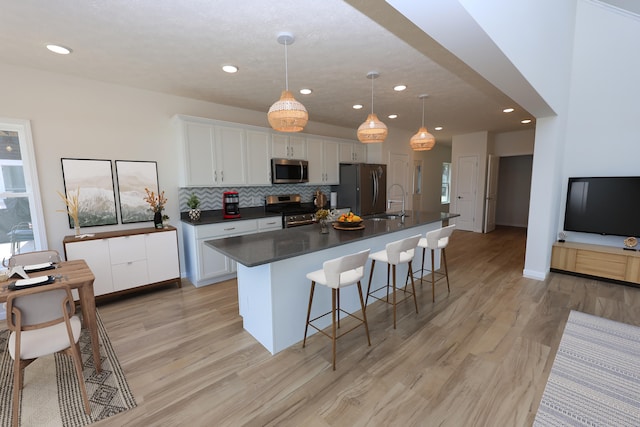 kitchen with white cabinets, appliances with stainless steel finishes, a center island with sink, and light hardwood / wood-style floors