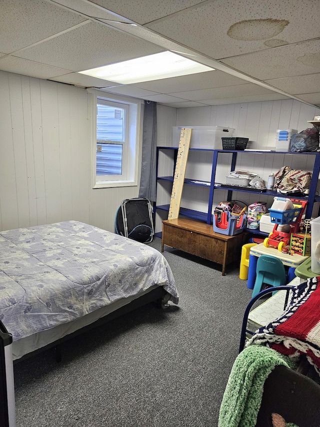 bedroom featuring carpet, a drop ceiling, and wood walls