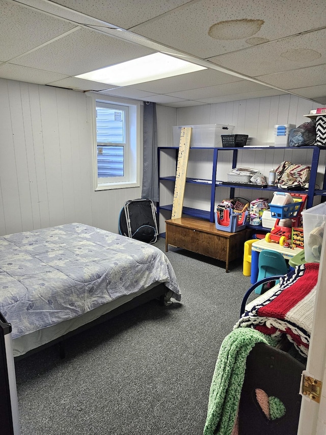 carpeted bedroom with a drop ceiling and wood walls