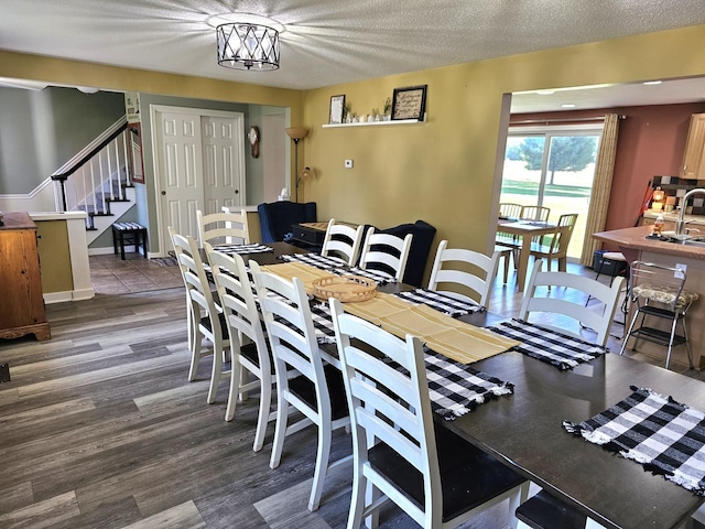 dining room with sink, dark wood-type flooring, a textured ceiling, and a notable chandelier