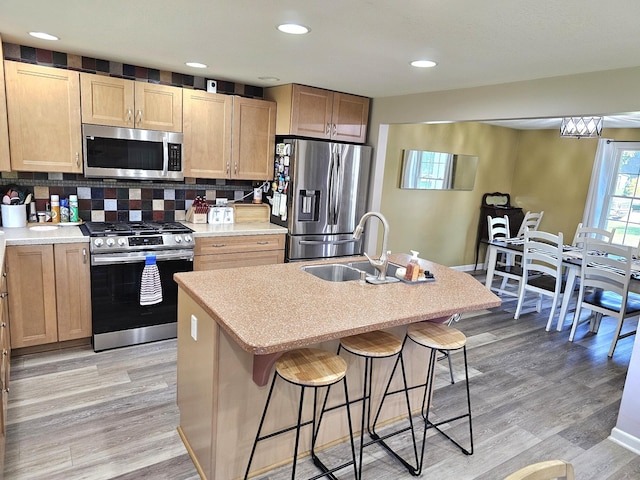 kitchen with a breakfast bar, backsplash, sink, an island with sink, and stainless steel appliances