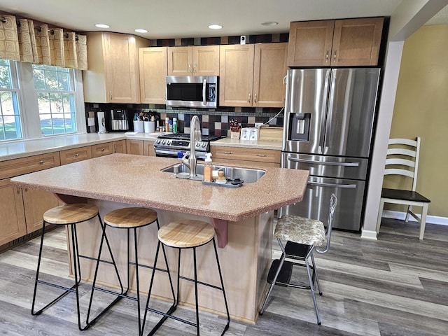 kitchen with decorative backsplash, a breakfast bar, hardwood / wood-style floors, and appliances with stainless steel finishes