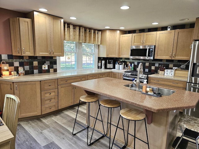 kitchen featuring a kitchen breakfast bar, stainless steel appliances, light hardwood / wood-style flooring, and an island with sink