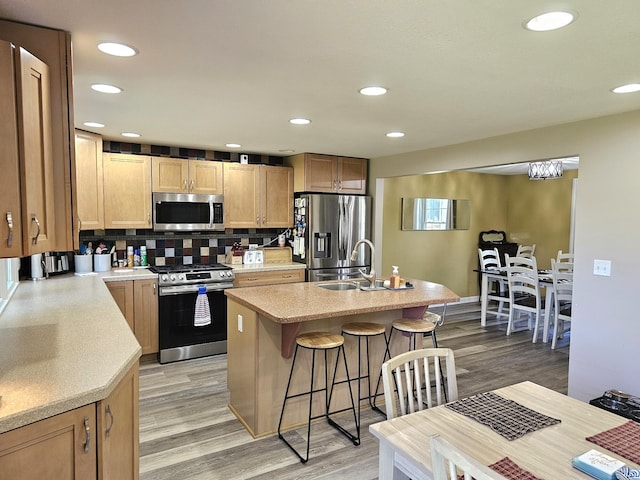 kitchen with sink, a center island with sink, light wood-type flooring, and appliances with stainless steel finishes