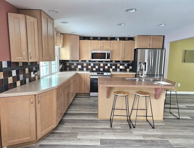 kitchen with backsplash, a kitchen bar, stainless steel appliances, and a kitchen island with sink