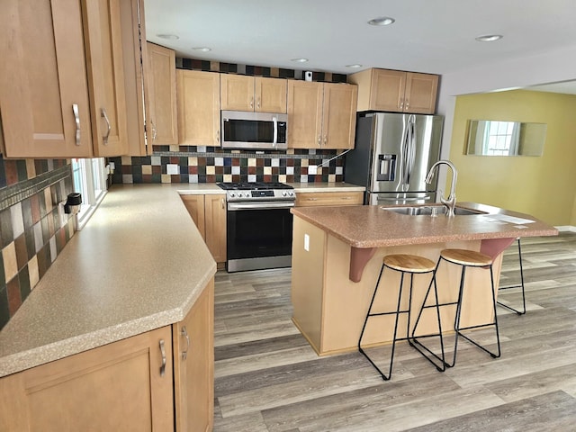 kitchen featuring tasteful backsplash, stainless steel appliances, sink, light hardwood / wood-style flooring, and an island with sink