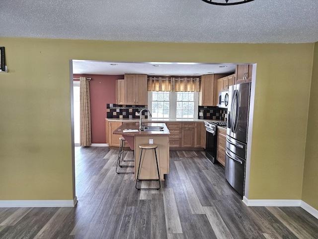 kitchen with a center island with sink, a textured ceiling, appliances with stainless steel finishes, tasteful backsplash, and a kitchen bar