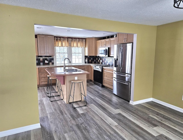 kitchen featuring a kitchen breakfast bar, sink, a textured ceiling, an island with sink, and stainless steel appliances