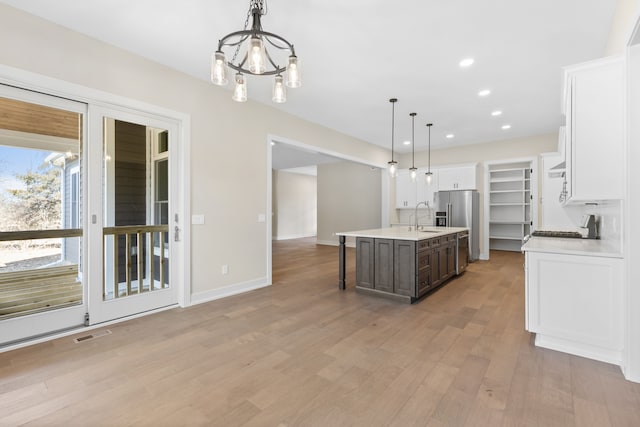 kitchen featuring light wood-type flooring, dark brown cabinets, decorative light fixtures, white cabinetry, and an island with sink