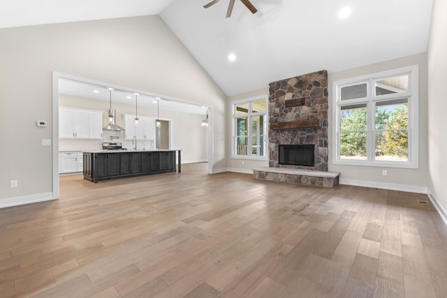 unfurnished living room with light hardwood / wood-style floors, high vaulted ceiling, ceiling fan, and a stone fireplace