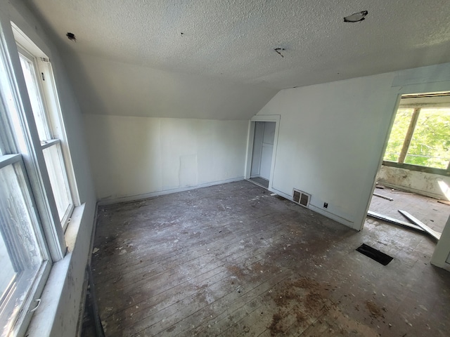 additional living space with a textured ceiling, dark hardwood / wood-style floors, and vaulted ceiling