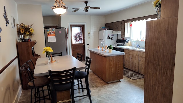 kitchen with a kitchen island with sink, black range with electric stovetop, ceiling fan, stainless steel fridge, and white fridge