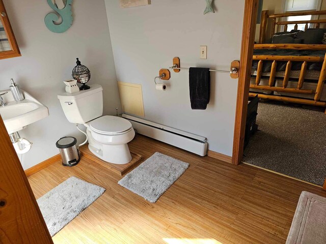 bathroom with hardwood / wood-style floors, a baseboard radiator, toilet, and sink