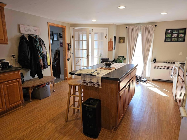 kitchen with radiator, french doors, a kitchen breakfast bar, light hardwood / wood-style floors, and a kitchen island