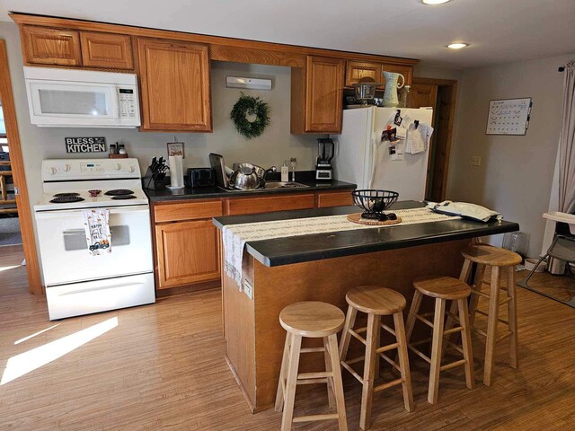 kitchen with a breakfast bar, a kitchen island, white appliances, and light wood-type flooring