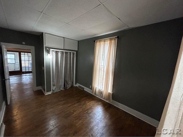 unfurnished room featuring a paneled ceiling, plenty of natural light, and dark wood-type flooring