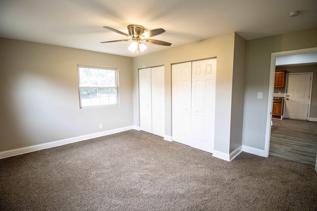 unfurnished bedroom featuring dark colored carpet, ceiling fan, and two closets