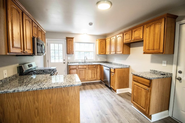 kitchen featuring stone counters, sink, kitchen peninsula, stainless steel appliances, and light hardwood / wood-style flooring