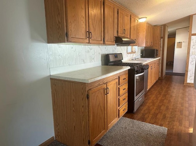 kitchen with stainless steel gas stove, sink, dark hardwood / wood-style flooring, backsplash, and a textured ceiling