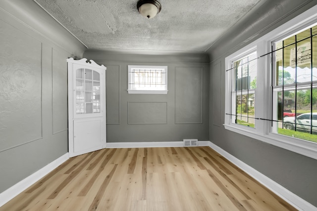 unfurnished room featuring a textured ceiling, light wood-type flooring, and plenty of natural light