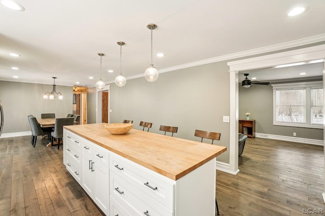 kitchen with a kitchen island, butcher block countertops, decorative light fixtures, white cabinets, and ornamental molding