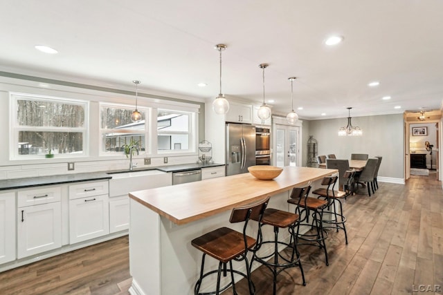 kitchen featuring a kitchen bar, decorative light fixtures, a center island, appliances with stainless steel finishes, and white cabinets