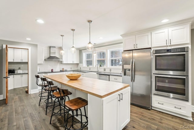 kitchen featuring stainless steel appliances, a kitchen island, wall chimney range hood, and white cabinets