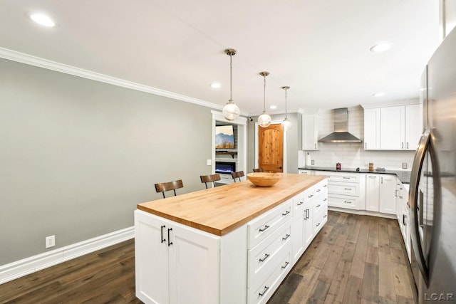 kitchen featuring butcher block countertops, white cabinetry, a center island, hanging light fixtures, and wall chimney range hood