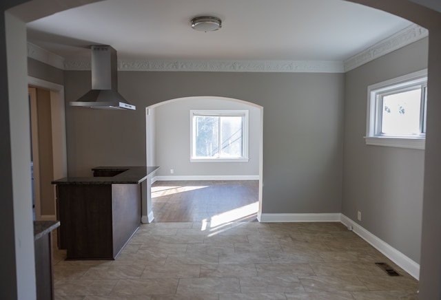 kitchen with dark stone countertops, wall chimney range hood, and ornamental molding