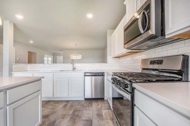 kitchen featuring hanging light fixtures, light hardwood / wood-style flooring, backsplash, white cabinets, and appliances with stainless steel finishes