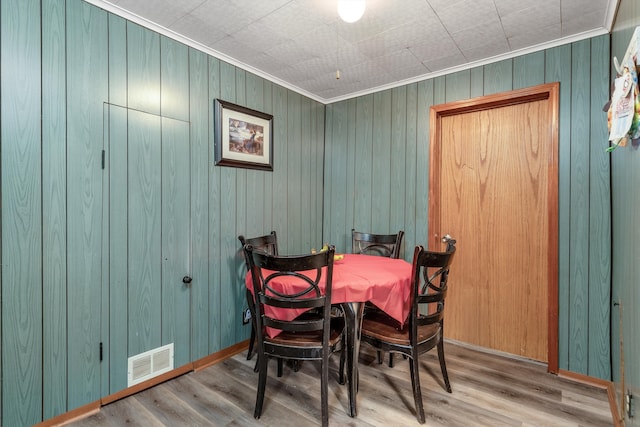 dining space with wood walls, wood-type flooring, and ornamental molding