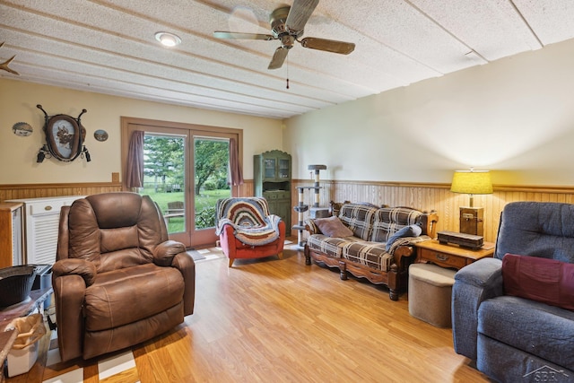 living room with hardwood / wood-style floors, ceiling fan, wood walls, and a textured ceiling