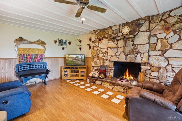 living room featuring hardwood / wood-style flooring, ceiling fan, a stone fireplace, and wooden walls