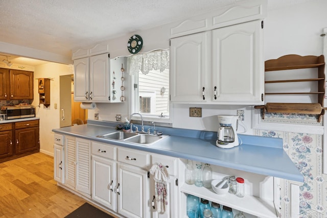 kitchen featuring white cabinets, light hardwood / wood-style floors, sink, and a textured ceiling