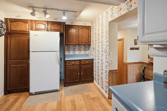 kitchen with wooden walls, light hardwood / wood-style flooring, a textured ceiling, and white refrigerator