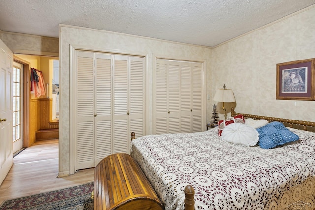 bedroom with two closets, a textured ceiling, and light wood-type flooring