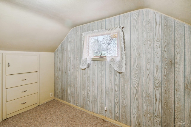 additional living space with wooden walls, light colored carpet, and vaulted ceiling