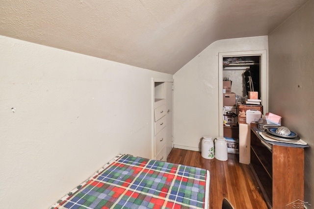 bedroom with a textured ceiling, a closet, dark hardwood / wood-style floors, and vaulted ceiling