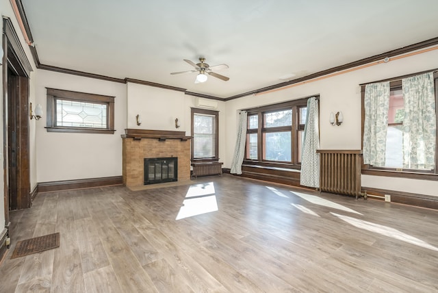 unfurnished living room featuring light wood-type flooring, a brick fireplace, ornamental molding, ceiling fan, and radiator heating unit