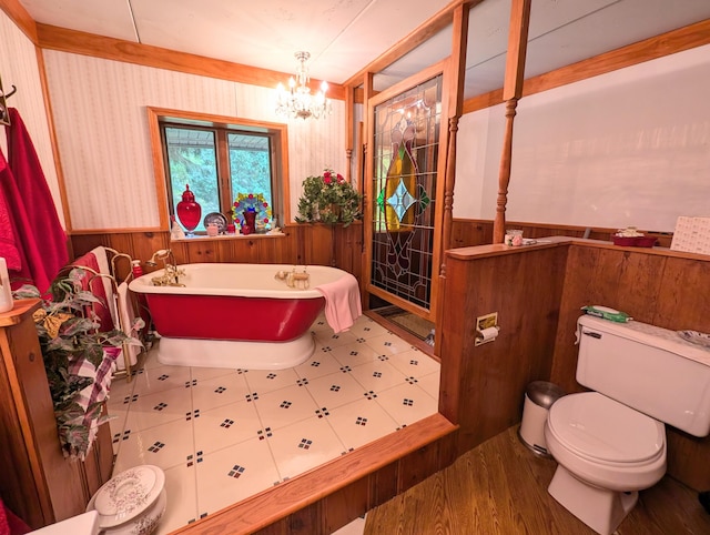 bathroom with a washtub, an inviting chandelier, toilet, and wooden walls