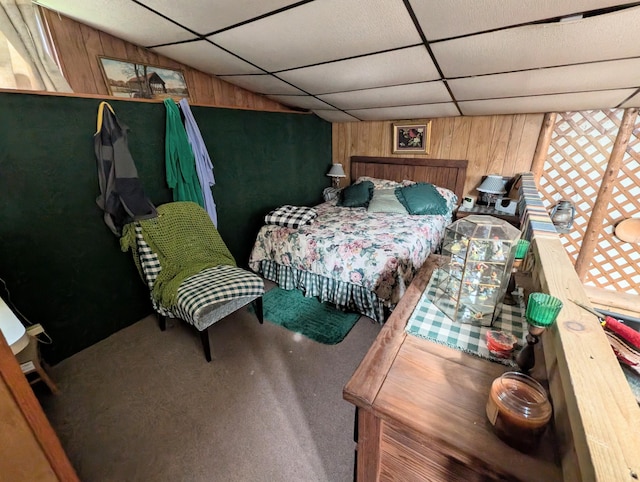 bedroom with carpet flooring, a drop ceiling, and wood walls