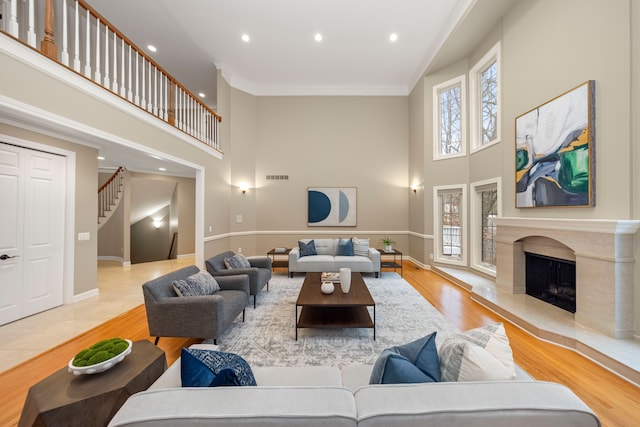 living room featuring light wood-type flooring, ornamental molding, a high ceiling, and a high end fireplace