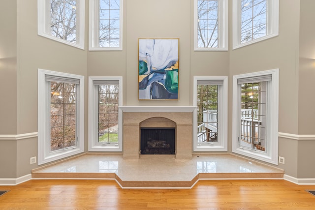 unfurnished living room with light hardwood / wood-style floors, a towering ceiling, and a high end fireplace