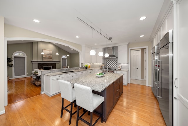 kitchen with a breakfast bar, white cabinets, sink, wall chimney exhaust hood, and a kitchen island